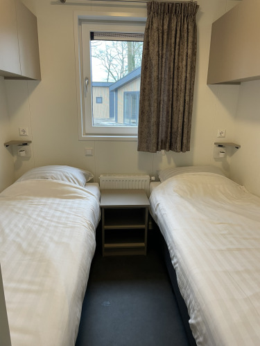 Zimmer mit zwei Einzelbetten, Nachttisch und Fenster im Wood Cottage, Holiday park De Witte Berg, Niederlande.