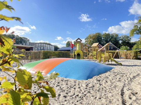 Playground with colorful jumping pillow and play structures at Wood Cottage + hot tub, De Witte Berg, Netherlands.