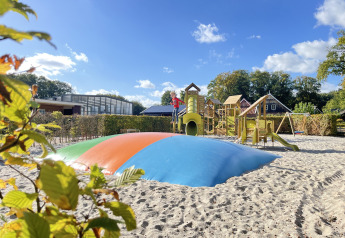Playground with colorful jumping pillow and play structures at Wood Cottage + hot tub, De Witte Berg, Netherlands.