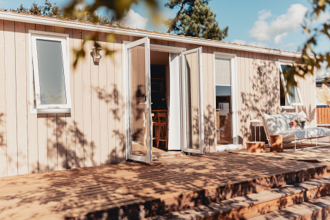 Glamping-verblijf met open deuren, houten terras en gezellige zithoek op een zonnige dag.