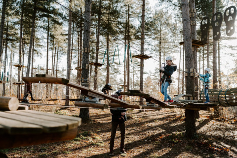 Kinder meistern einen Hochseilgarten bei Hobbit House, Cosy Cabins, im Wald von Limburg, Belgien, mit Helmen.