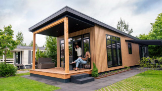 Twee mensen ontspannen op de veranda van een moderne Sunlodge, omgeven door tuin en bomen.