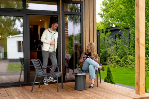 Due persone si rilassano su una terrazza in legno della Sunlodge all'Holiday Park 't Rheezerwold, Paesi Bassi.