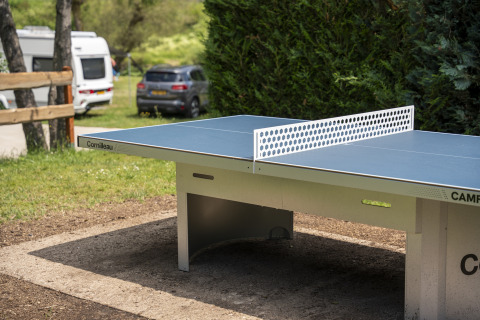 Outdoor ping pong table at Camping du Rivage in Diekirch, Luxembourg, surrounded by greenery and campers.