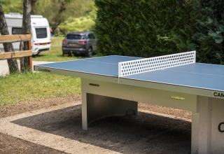 Buitentafeltennistafel op Camping du Rivage in Diekirch, Luxemburg, omgeven door groen en kampeerwagens.