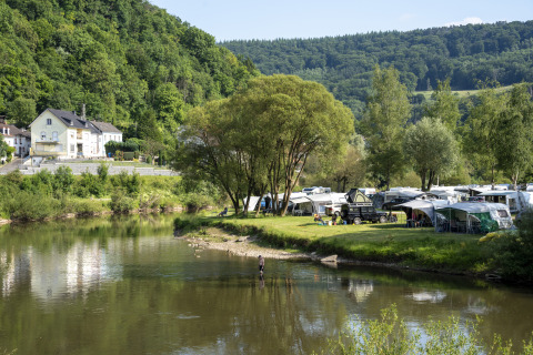 Riverside campsite with tents and caravans, lush green hills, and trees at Diekirch, Luxembourg holiday park.