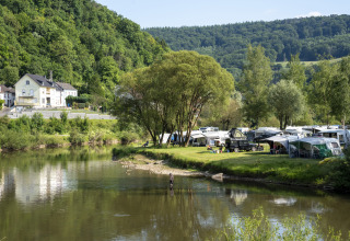 Campingplads ved floden med telte og campingvogne, grønne bakker og træer i Diekirch, Luxembourg.