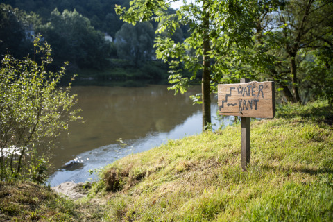 Skilt ved vandkanten i campingområdet Camping du Rivage, Diekirch i Luxembourg, med frodige træer.