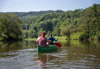 Two people canoeing together on a calm river surrounded by lush hills at Diekirch, Luxembourg.
