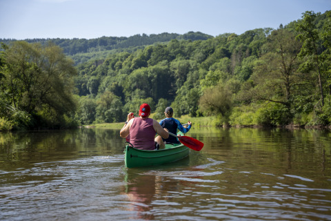 Two people canoeing together on a calm river surrounded by lush hills at Diekirch, Luxembourg.