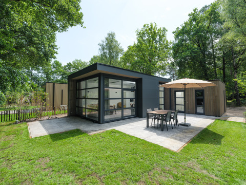 Moderne Bosvilla Comfort Lodge mit großen Fenstern, Terrasse, Sonnenschirm und Esstisch im Grünen.