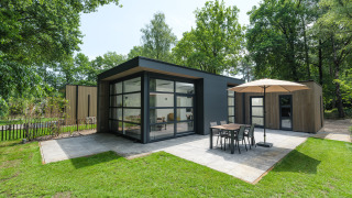 Moderne Bosvilla Comfort Lodge mit großen Fenstern, Terrasse, Sonnenschirm und Esstisch im Grünen.