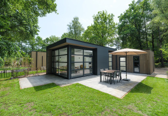 Moderne Bosvilla Comfort Lodge mit großen Fenstern, Terrasse, Sonnenschirm und Esstisch im Grünen.