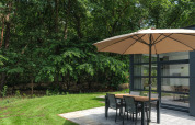 Terrasse mit Sonnenschirm und Esstisch bei Bosvilla Comfort im Veluwepark de Bosgraaf, Niederlande.