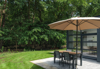 Terrasse mit Sonnenschirm und Esstisch bei Bosvilla Comfort im Veluwepark de Bosgraaf, Niederlande.