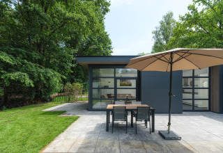 Moderne Lodge mit Terrassentisch, Sonnenschirm und Garten im Veluwepark de Bosgraaf, Niederlande.