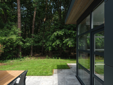 Blick von Bosvilla Comfort im Veluwepark de Bosgraaf, Niederlande, auf Terrasse, Rasen und Wald.