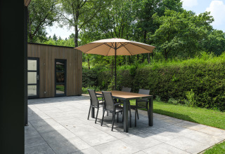 Terrasse bei Bosvilla Comfort im Veluwepark de Bosgraaf, Niederlande, mit Tisch, Stühlen und Sonnenschirm.