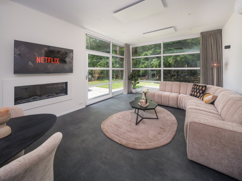 Moderne woonkamer in Bosvilla Comfort in Veluwepark de Bosgraaf, Nederland, met ruime zetel en tuinzicht.
