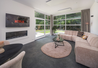 Modernes Wohnzimmer in der Bosvilla Comfort im Veluwepark de Bosgraaf, Niederlande, mit großer Couch und Blick ins Grüne.