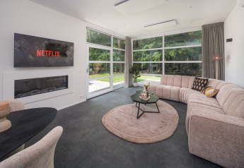 Modernes Wohnzimmer in der Bosvilla Comfort im Veluwepark de Bosgraaf, Niederlande, mit großer Couch und Blick ins Grüne.