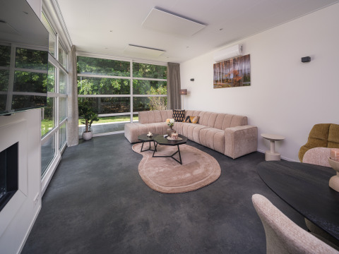 Modernes Wohnzimmer in der Bosvilla Comfort im Veluwepark de Bosgraaf mit großen Fenstern und eleganter Einrichtung.
