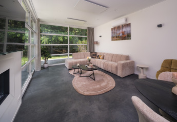 Salon élégant de la Bosvilla Comfort au Veluwepark de Bosgraaf, Pays-Bas, avec grandes fenêtres et décoration moderne.
