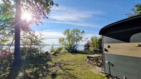 Zicht op het meer en het bos bij Tiny Wagon in Marina Parcs Almere met zon en buitenzitplekken.