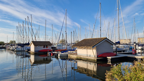 Boten en chalets bij Marina Parcs Almere in Nederland, weerspiegeld in het rustige water en blauwe lucht.