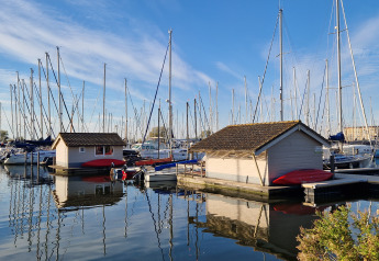 Boats and chalets at Marina Parcs Almere in the Netherlands, with reflections in calm water and clear sky.