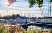 Sunny scene at Chalets at Marina Parcs Almere, Netherlands, with sailboats, houseboats, and lush greenery.