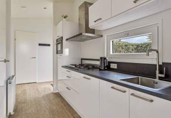 Modern white kitchen in a Natuurlodge at Recreatiepark het Esmeer, Netherlands, featuring a sink and stove.