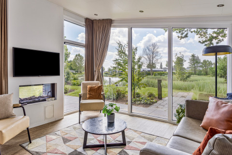 Salon moderne de la Natuurlodge au Recreatiepark het Esmeer avec grandes baies et vue sur la nature.