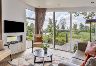 Moderne woonkamer in Natuurlodge bij Recreatiepark het Esmeer met grote ramen en uitzicht op de natuur.