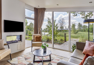 Salón moderno en Natuurlodge, Recreatiepark het Esmeer, Países Bajos, con ventanales y vistas a la naturaleza.