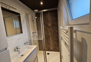 Moderne badeværelse med brusekabine, vask, stort spejl, radiator og vindue i Bos Cottage, De Thijmse Berg.