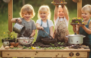 Four kids play together at an outdoor mud kitchen, making mud pies and smiling at Boerderij huisje safari tent.