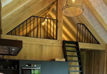 Interieur van een safaritent met houten balken, mezzanine en zwarte ladder in Beloofde Land, Nederland.