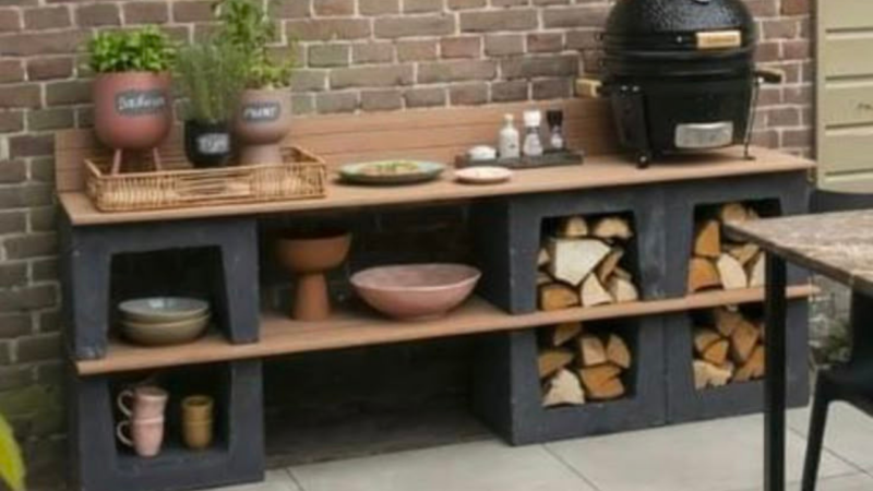 Outdoor-Küchenbank mit Kräutertöpfen, Grill, Geschirr und Brennholz vor einer Ziegelmauer aufgestellt.