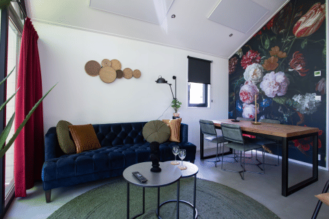 Moderne stue i Eco Cottage, De Thijmse Berg, med mørkeblå sofa, blomster-vægmaleri og træbord.