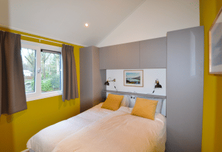 Bedroom in the Eco Cottage at De Thijmse Berg, Netherlands, with yellow walls, double bed and windows.