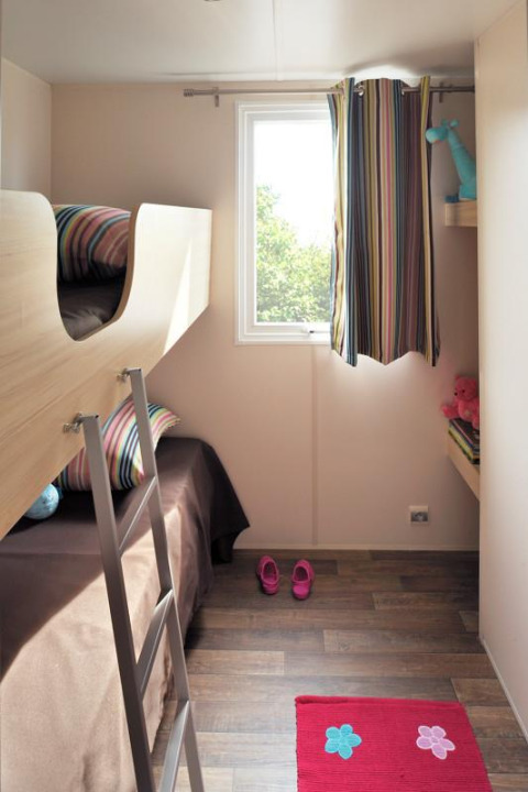 Cameretta in una tenda safari Cabane Nature con letto a castello, finestra e decorazioni colorate.