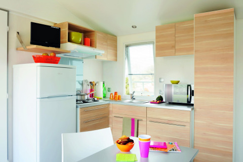 Moderne køkken i Stacaravan Confort på Flower Camping Au Bois Des Biches i Frankrig med lyst træ og hvide apparater.