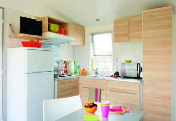 Moderne Küche in der Stacaravan Confort im Flower Camping Au Bois Des Biches, Frankreich, mit hellen Holzmöbeln.