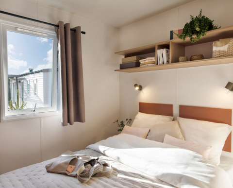 Lichte slaapkamer in Stacaravan Confort bij Flower Camping Au Bois Des Biches, Frankrijk, met raam en planken.