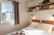 Lichte slaapkamer in Stacaravan Confort bij Flower Camping Au Bois Des Biches, Frankrijk, met raam en planken.