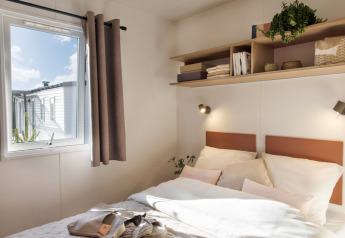 Lichte slaapkamer in Stacaravan Confort bij Flower Camping Au Bois Des Biches, Frankrijk, met raam en planken.