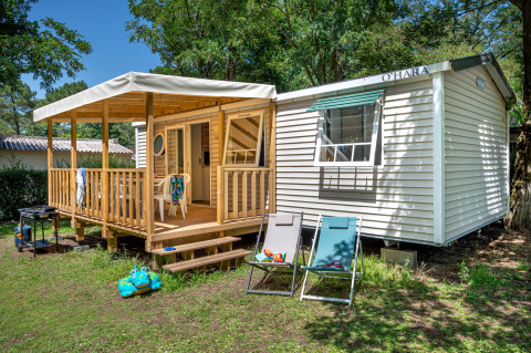 Rustige Stacaravan Confort chalet met houten terras, tuinstoelen en grasrijke tuinomgeving.