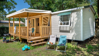 Rustige Stacaravan Confort chalet met houten terras, tuinstoelen en grasrijke tuinomgeving.