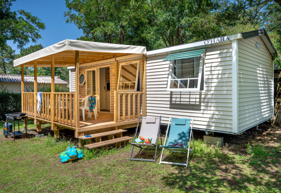 Rustige Stacaravan Confort chalet met houten terras, tuinstoelen en grasrijke tuinomgeving.